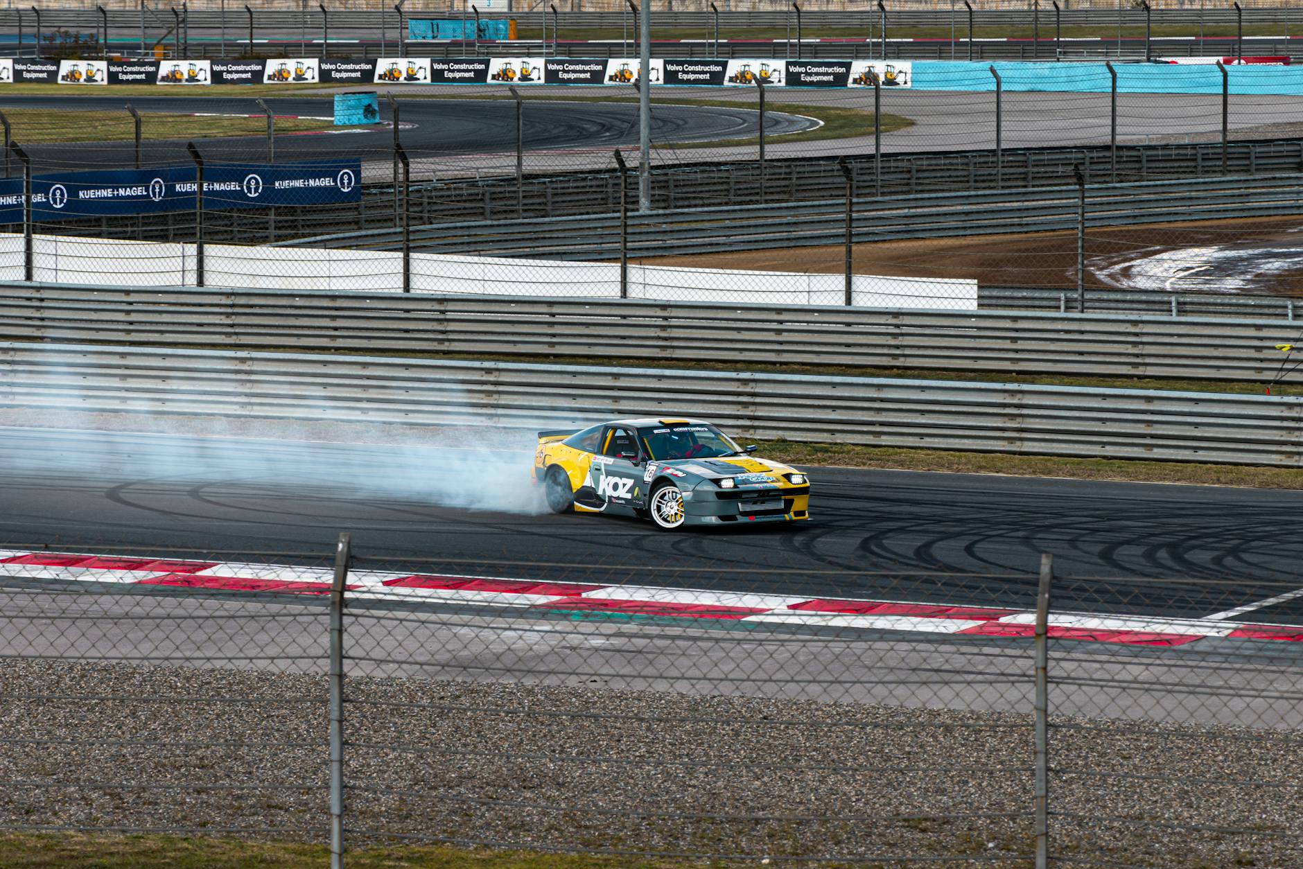 Aston Martin Vantage w drifcie na torze, z kłębem dymu zza kół