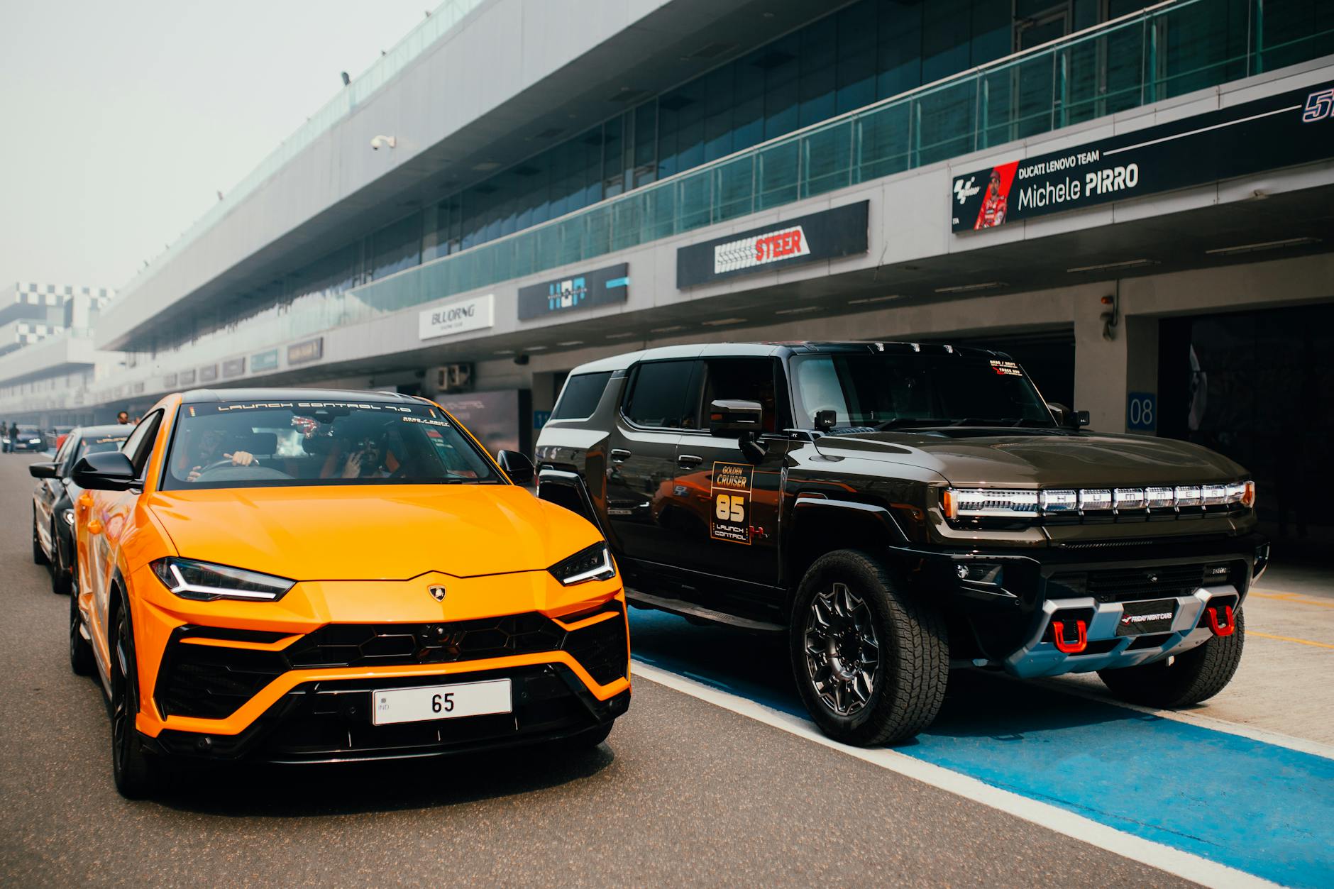 Pomarańczowe Lamborghini i czarny SUV zaparkowane na torze wyścigowym