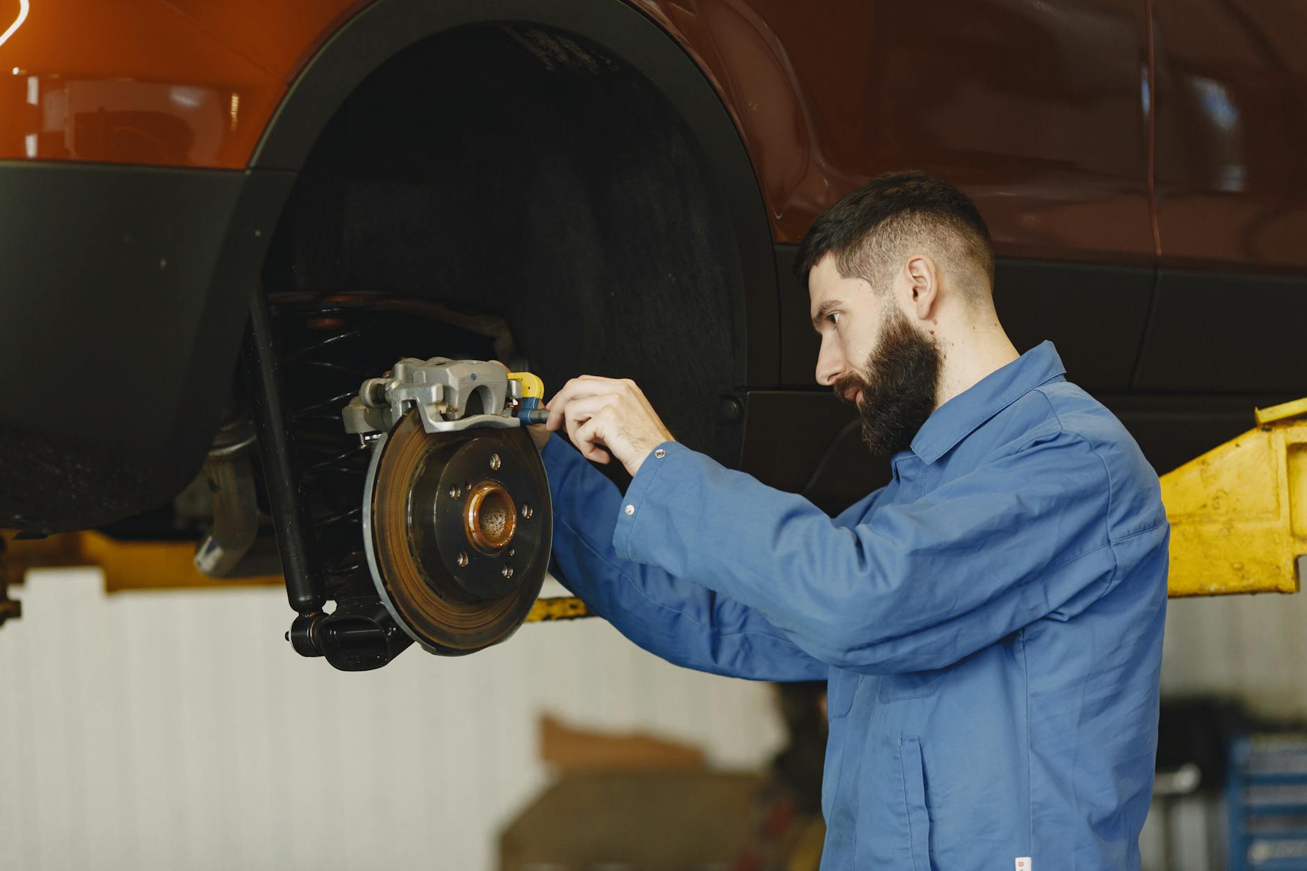 Mechanik w niebieskim kombinezonie naprawia hamulce w aucie w warsztacie