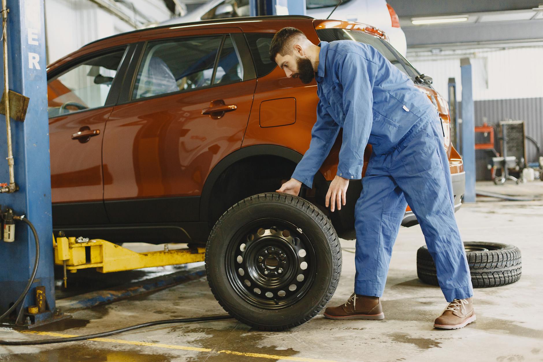 Mechanik w niebieskim kombinezonie wymienia koło w czerwonym SUV-ie Dacii