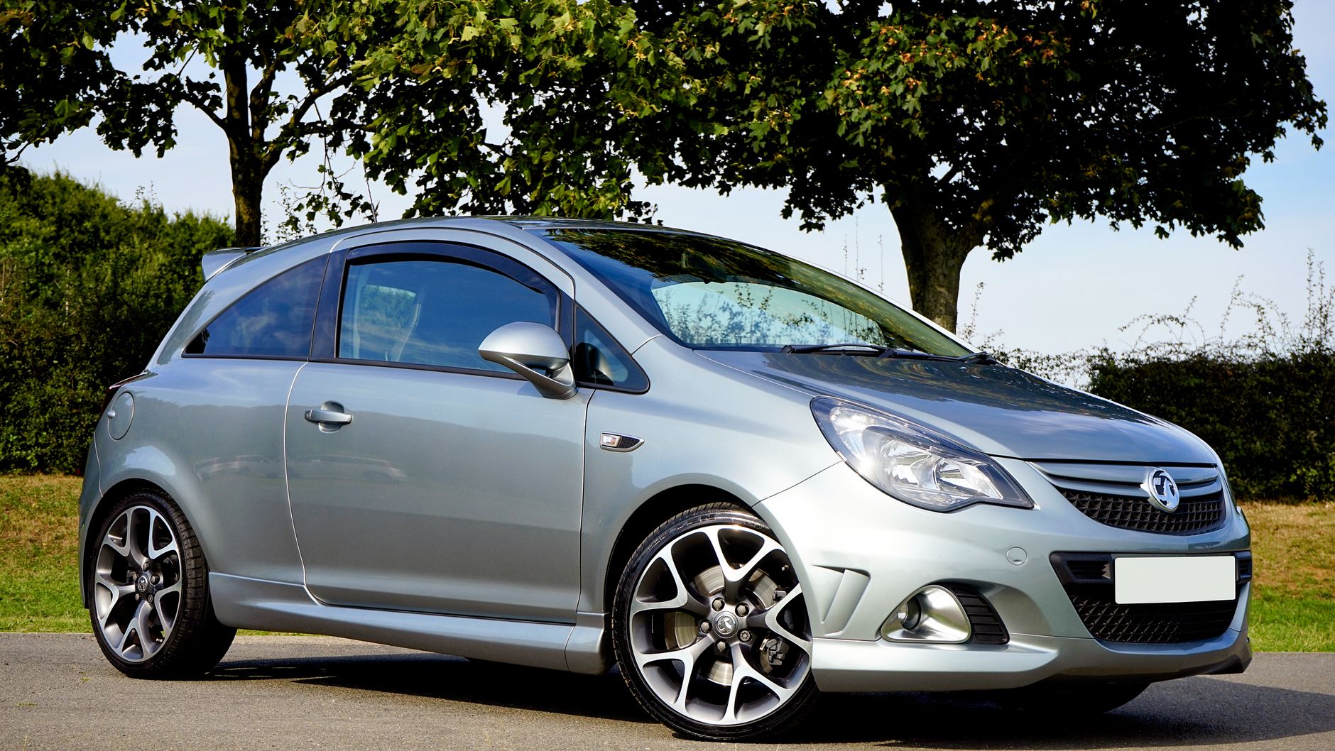 Srebrny Ford Fiesta hatchback zaparkowany w słońcu na tle drzew