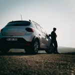Mężczyzna oparty o samochód Dacia na malowniczej drodze o zachodzie słońca